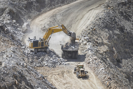 Santa Lucia de Gordon, Spain: View of a large yellow excavator parked in a quarry under a clear blue sky.