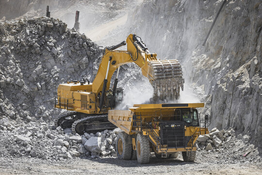 Santa Lucia de Gordon, Spain: View of a large yellow excavator parked in a quarry under a clear blue sky.