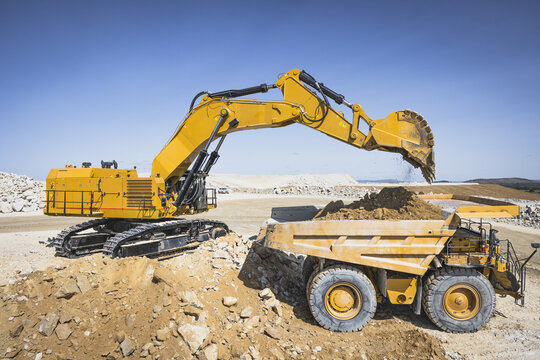 Santa Lucia de Gordon, Spain: View of a large yellow excavator parked in a quarry under a clear blue sky.