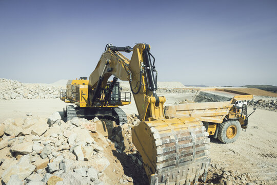 Santa Lucia de Gordon, Spain: View of a large yellow excavator parked in a quarry under a clear blue sky.
