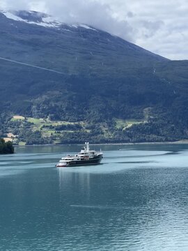 Luxury yacht anchored in turquoise lake with snow-capped mountain in Loen, Norway