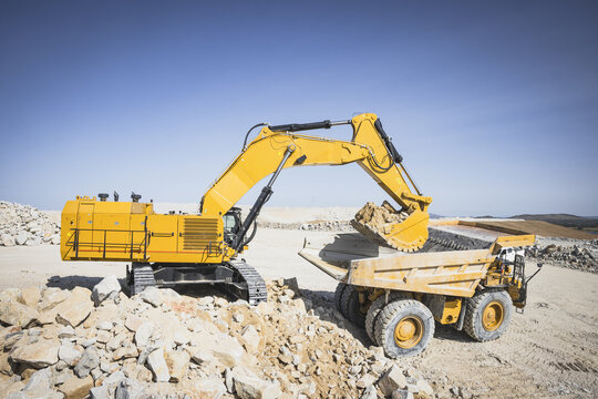 Santa Lucia de Gordon, Spain: View of a large yellow excavator parked in a quarry under a clear blue sky.