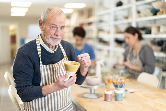 Elderly potter demonstrates a clay cup he made with his own hands