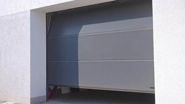 Garage door opening while hand presses remote control outside house. Concept of residential garage access and automatic door operation