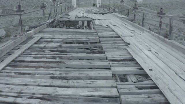 Dilapidated bridge in foggy setting. Decaying wooden structure over misty industrial area. Worn out wooden bridge with gaps and rusted supports over foggy industrial terrain
