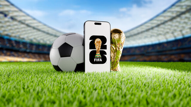 Mobile phone with 2026 FIFA World Cup Logo on Green Grass of a Modern Football Stadium with Trophy and Ball.