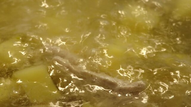Boiling pot with diced potatoes and meat simmering in broth, bubbles rising to the surface, creating a rich and inviting texture in a kitchen setting