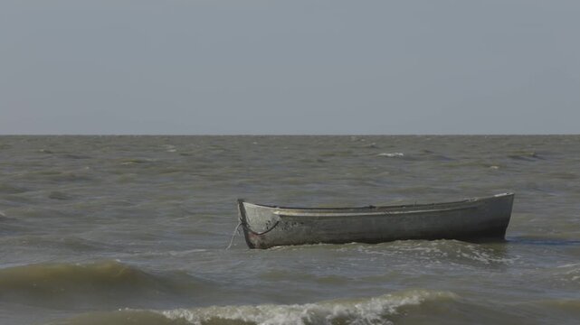 Seafarer on waves. Weathered skiff battles choppy waters under cloudy skies. Ancient boat traverses rolling sea with barnacle covered hull amid muted atmospheric conditions
