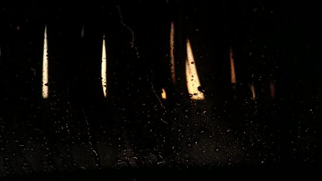 Water droplets cascade down a dark glass surface, revealing illuminated vertical lines in the background, creating a mesmerizing interplay of light and shadow