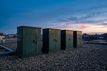 Fototapeta premium Row of dark green utility boxes on a gravel rooftop under a colorful twilight sky