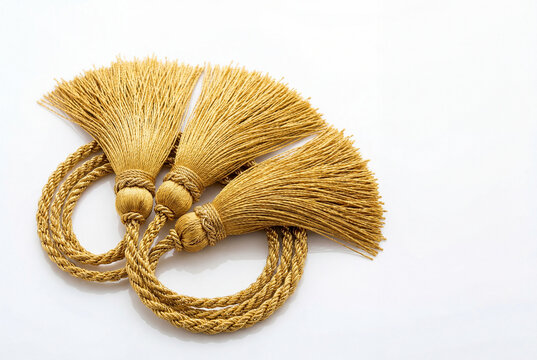 Three ornate gold fabric tassels resting on a plain white surface