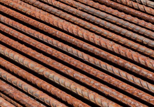 Close-up view of numerous parallel rusty steel reinforcing bars, showing textured surfaces and orange-brown corrosion.