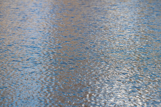 Calm bluegray water with patterns. Captivating water texture with gentle sheen and waves. Abstract water surface emphasizing subtle patterns and soft light reflections