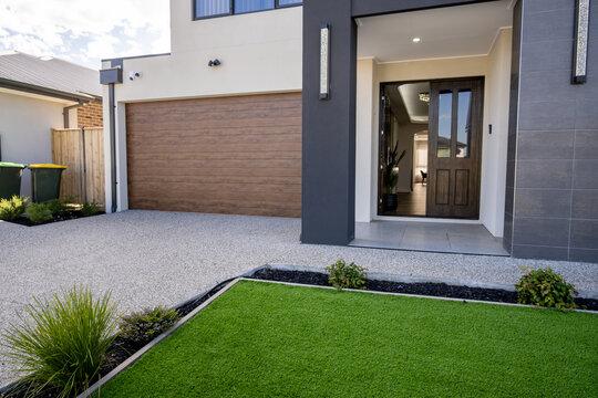 Front facade of a modern two-storey Australian home with garage,&nbsp;front entry door,&nbsp;artificial grass lawn bordered by exposed aggregate concrete driveway. Landscaping typical of new housing estates