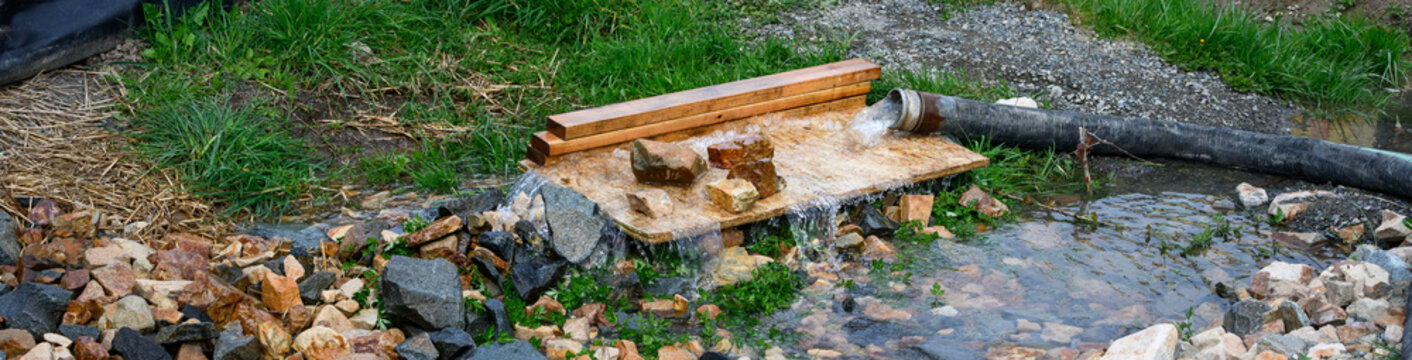 Commercial construction site, heavy duty industrial hose dewatering, pumping excess water out of job site, plywood and rock used to prevent ground erosion
