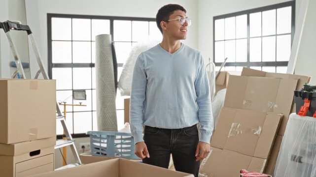 Man raises arms among stacked moving boxes inside building, smiling upward while unpacking and stretching; fresh start joy.