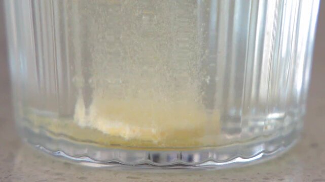 Effervescent tablet dissolving in water glass closeup showing fizzy bubbles and vitamin release motion.