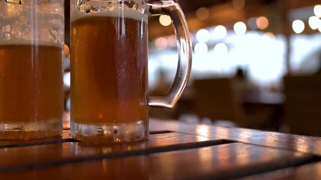 Close up of two frothy beer mugs on a wooden table with soft bokeh background lights.