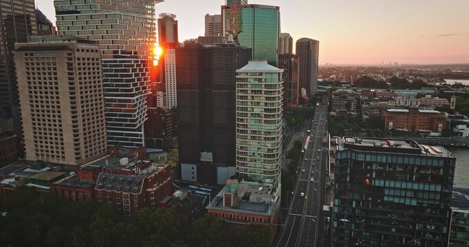 Sydney Central Business District skylines modern skyscrapers, vibrant city architecture, and busy traffic flowing along a main road, all glowing under the warm light of a beautiful sunset. Aerial shot
