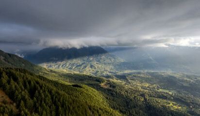 Fototapeta premium Dramatic Cloudscape Over Forested Mountain Valley in British Columbia, Canada With Sunlit Ridges