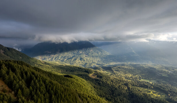 Dramatic Cloudscape Over Forested Mountain Valley in British Columbia, Canada With Sunlit Ridges