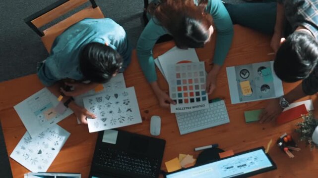 Top view of project manager writing idea while team joining meeting and talking about idea. Professional designer design logo while looking at color palette and writing idea down in paper. Symposium.