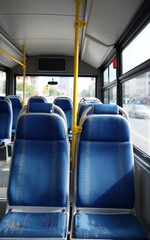 Naklejka premium Empty bus interior with blue seats yellow poles and city view through