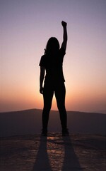 Fototapeta premium Silhouetted figure stands atop hill arms raised in triumph against