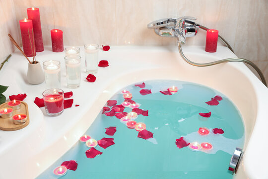 Romantic atmosphere. Bathtub with burning candles, petals and air reed freshener in bathroom, closeup