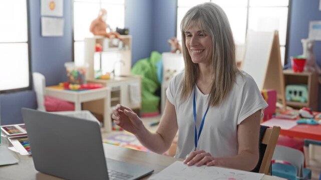 Woman teacher holds abc drawing and smiles while waving hand during online lesson in classroom; early learning joy.