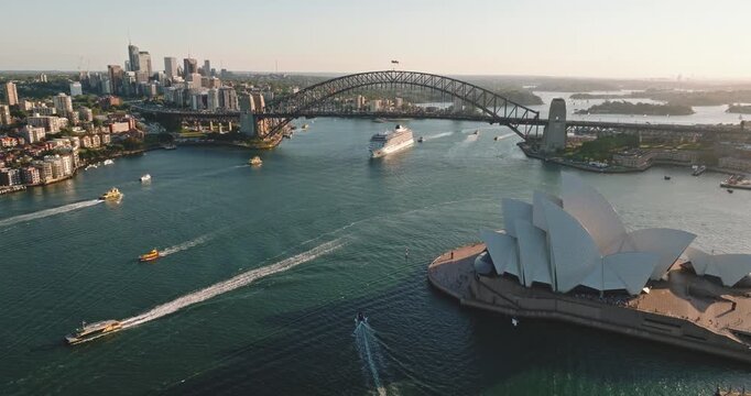 Sydney Harbour aerial view featuring the Opera House and Harbour Bridge with a cruise ship and ferries navigating the busy, sunlit waterway, capturing travel and city life
