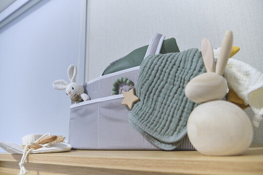 Baby changing organizer bag with soft muslin blanket and wooden toys on a light wooden shelf