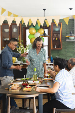 Diverse multigenerational family with seniors sharing festive meal in kitchen, holding wine glasses