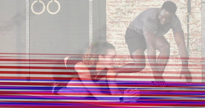 Stretching woman in sportswear wearing tracker reaching forward on mat at gym, man assisting, rings