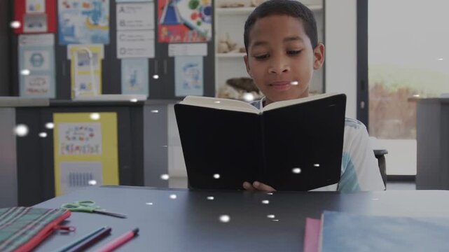 Student boy opening black book, reading in classroom, white particles floating across boy for study