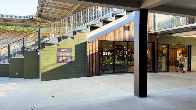 Walkway through stadium entrance with colorful seating and shops at sunny day.
