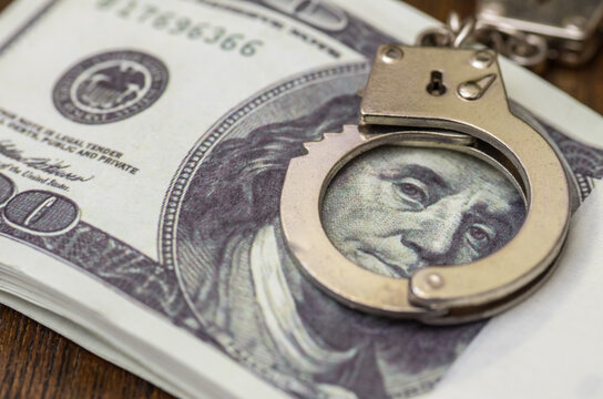Financial Crime and Corruption Concept with Pair of Handcuffs Over Stack of One Hundred Dollar Bills Featuring Benjamin Franklin