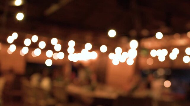 Blurred outdoor night party with warm string lights glowing in tropical restaurant ambiance and evening motion.