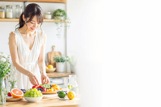 Smiling Woman Preparing Fresh Fruits in Bright Kitchen
,キッチンでフルーツを盛り付ける笑顔の女性　健康的なライフスタイルイメージ
