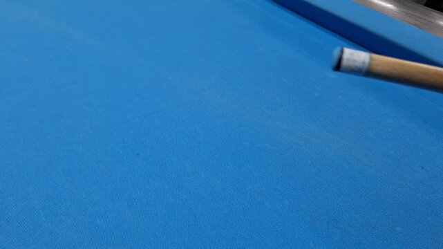 Close up of a wooden pool cue stick hitting a white billiard ball on a blue felt table in dynamic motion during a game
