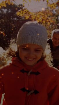 Vertical video: Child stepping parents playing in park, leaves and sparks floating around for ads