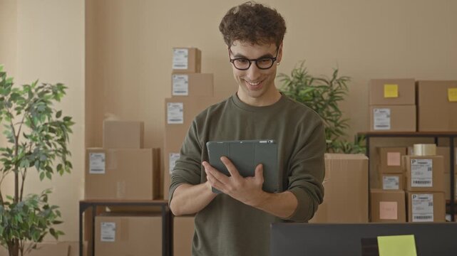 Man holding tablet, hands visible, tapping screen amid stacked cardboard packages in a packing area inside a building; small business efficiency.