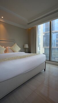 Bright and elegant hotel suite interior showing a neatly made double bed, glossy tiled floors, and a stunning view of urban architecture.