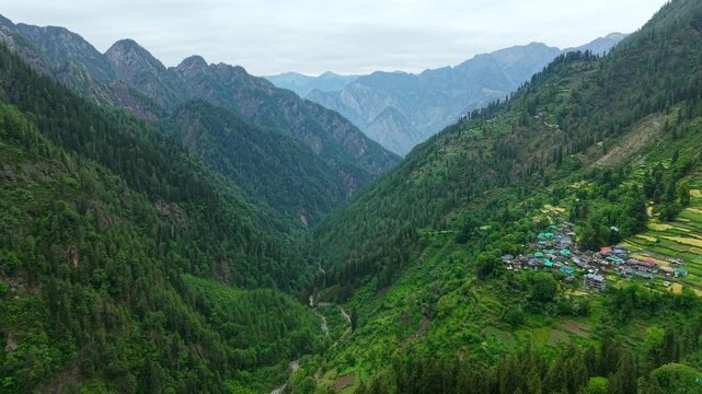 Dolly in aerial into deep Himalayan valley toward Grahan village on hillside with forest and layered mountains