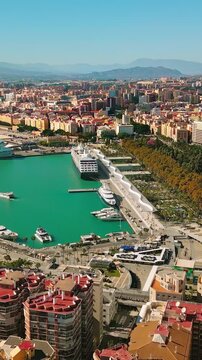 Vertical aerial pan from M&aacute;laga Port and Muelle Uno to dense city skyline on a clear sunny Mediterranean day, Spain