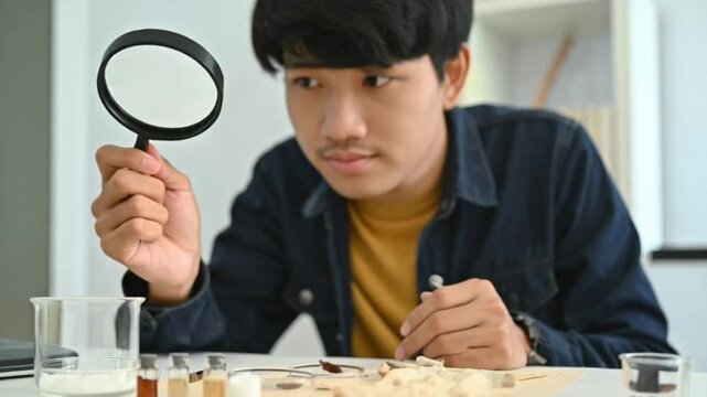 Young man examining small objects with magnifying glass in a lab setting