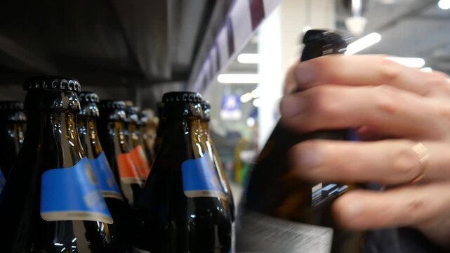 An elderly man choosing a bottle of beer in a supermarket