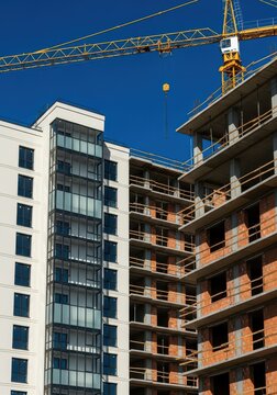Construction site features a yellow tower crane looming over a partially completed apartment building against a clear blue sky.