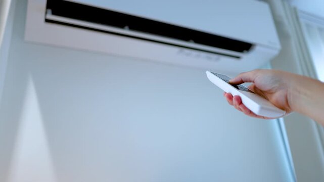 Hand Holding Remote Control to Adjust Wall Mounted Air Conditioner Unit