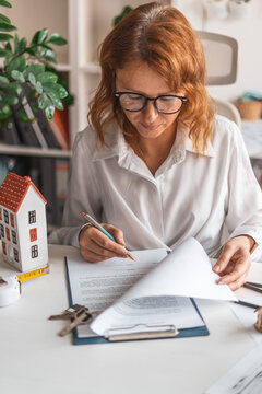 Young realtor consulting customer desk with housing documents, blueprint, miniature house. Signing rental sales agreement, professional property service, secure investment process. Signing contract.